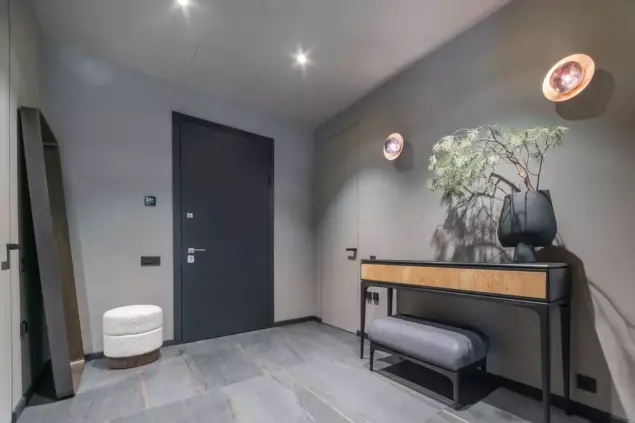 Um hall de entrada com cores neutras na parede, decoração moderna com um console, plantas e iluminação ambiente aconchegante, ideal para cores de tinta para hall de entrada.