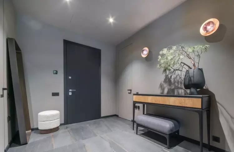Um hall de entrada com cores neutras na parede, decoração moderna com um console, plantas e iluminação ambiente aconchegante, ideal para cores de tinta para hall de entrada.