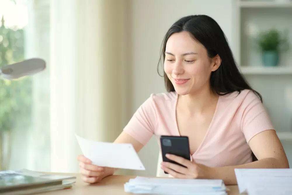 Mulher sorridente verificando documentos importantes com o celular.