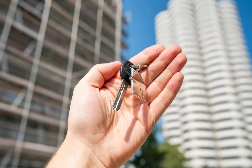 Mão segurando chaves de imóvel com prédio ao fundo, simbolizando financiamento conjunto para compra de imóveis.