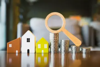 Imagem de casas em miniatura, moedas empilhadas e uma lupa