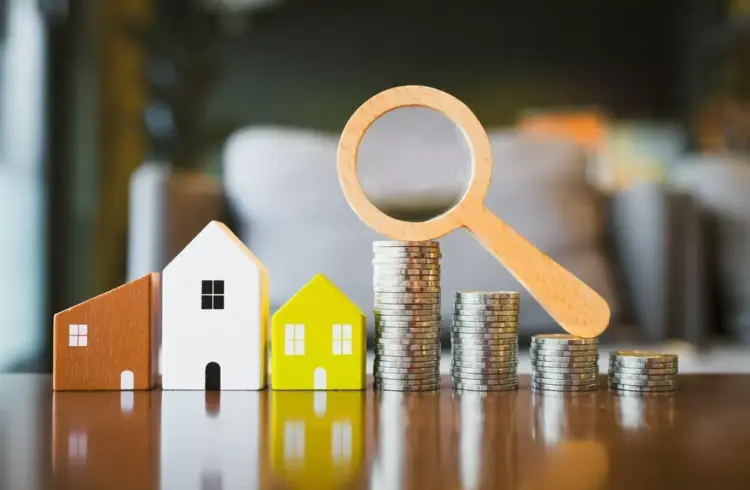 Imagem de casas em miniatura, moedas empilhadas e uma lupa