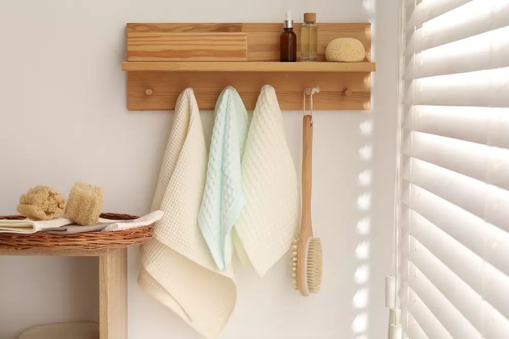 Organizar o espaço com toalhas de banho e acessórios de banho em um ambiente clean, com prateleira de madeira, escova de banho, e iluminação suave.