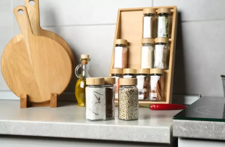 Organizar temperos em pote de vidro com tampas de madeira, com especiarias coloridas, utensílios de cozinha de madeira e bancada limpa.