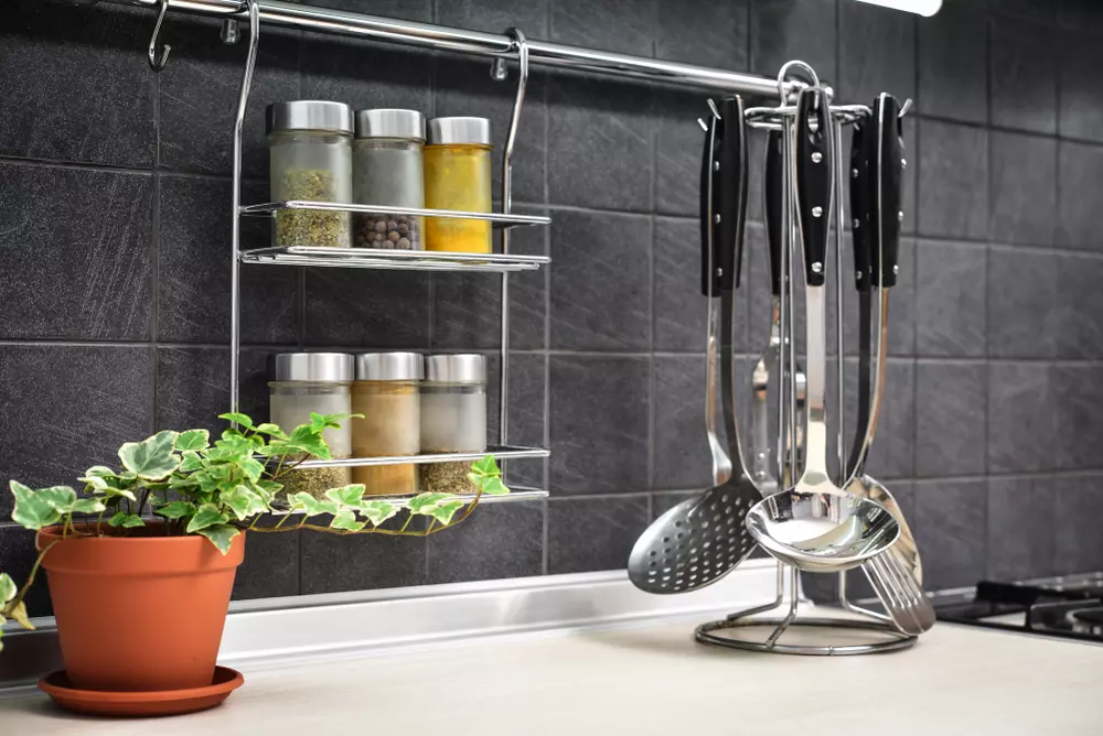 Organizar temperos em potes transparentes e utensílios de cozinha pendurados na parede, com planta verde na cozinha moderna.