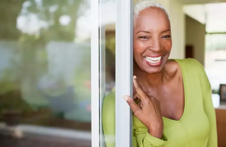 Mulher sorridente observando uma porta de correr de vidro na sua casa, destacando a praticidade e elegância desse tipo de porta moderna.