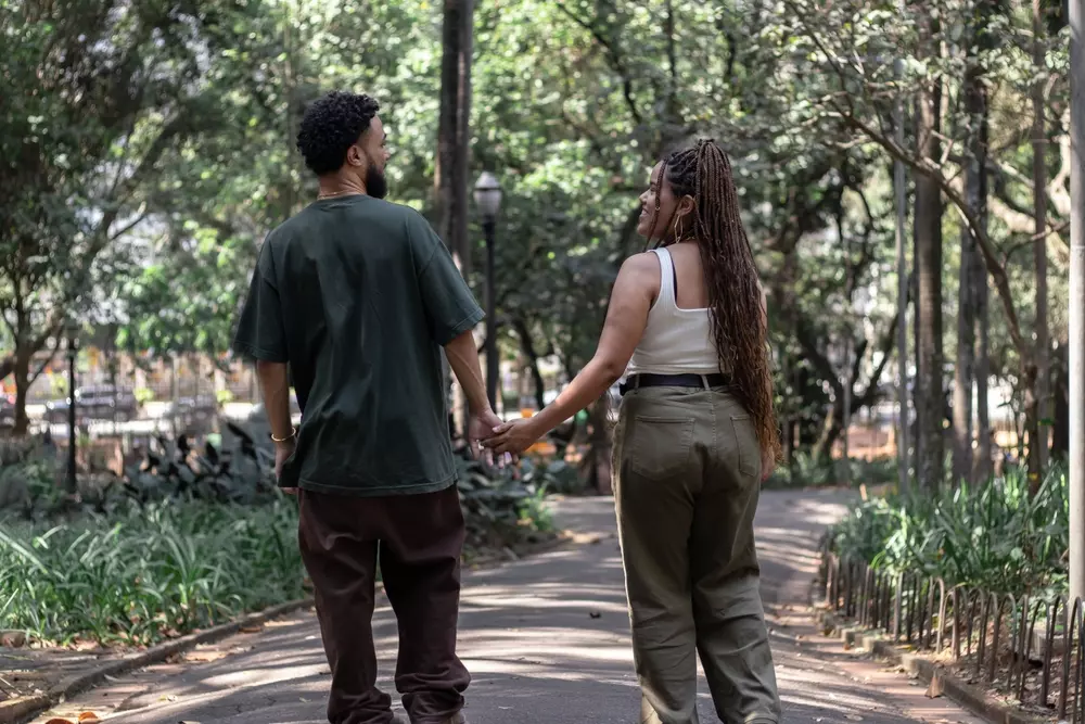 Casal caminhando de mãos dadas no parque, simbolizando os cinco tipos de riqueza na vida, como tempo, relacionamentos, saúde, conhecimento e espiritualidade, promovendo a ideia de aproveitar a vida ao máximo.