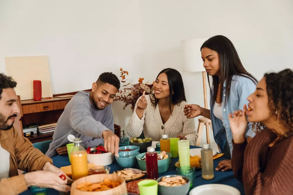 Grupo de amigos celebrando uma reunião social com comida e bebidas, mostrando a importância das relações e conexões humanas, evidenciando a riqueza social.