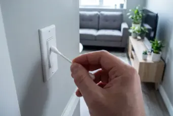 Pessoa limpando interruptor com cotonete, foco em cuidados com tomadas e interruptores