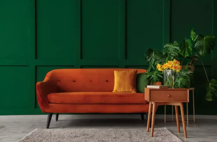 Sofá laranja com almofada amarela em sala decorada com móveis coloridos, parede verde e planta, representando tendência de móveis coloridos em 2026.