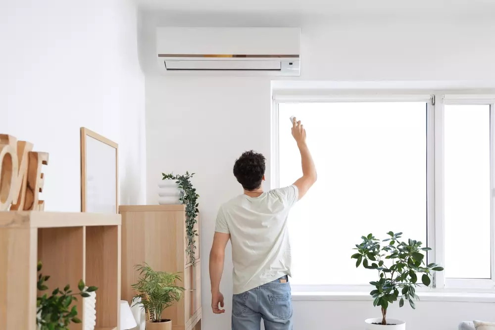 Homem ajustando o ar-condicionado para economizar energia elétrica, deixando o ambiente mais eficiente e reduzindo custos de energia.