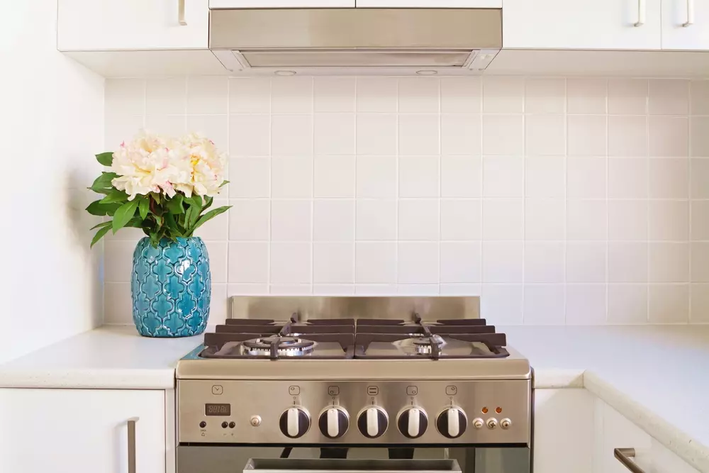 Um fogão de aço inox na cozinha moderna, com uma bancada branca, destaque para as vantagens do fogão como praticidade, eficiência e design elegante.