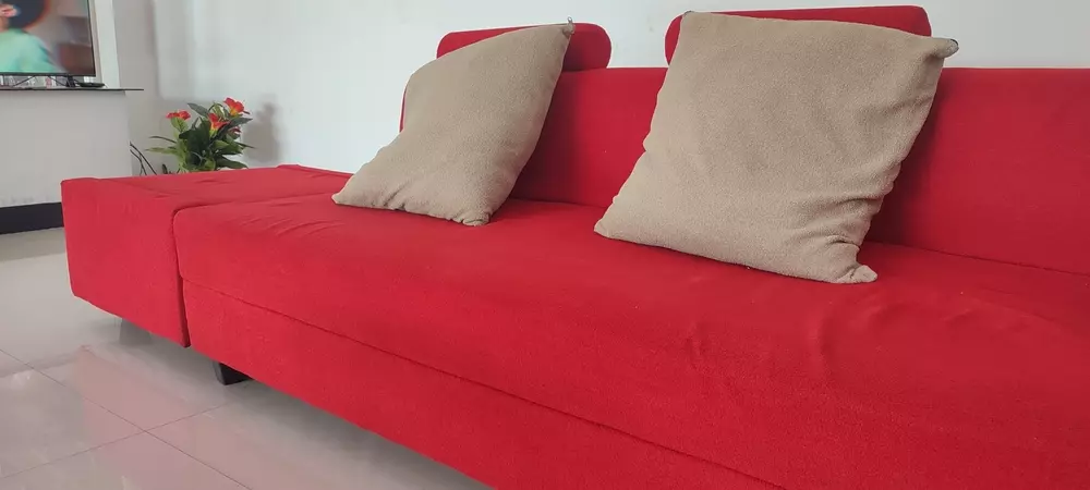 Sofá vermelho moderno com duas almofadas bege na decoração de sala de estar, perfeita para ambientes aconchegantes e elegantes.