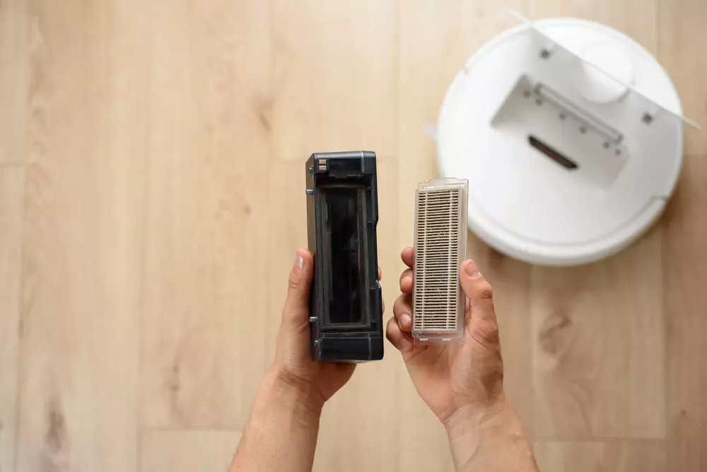Mãos masculinas retiram um filtro HEPA sujo de um aspirador robô após a limpeza