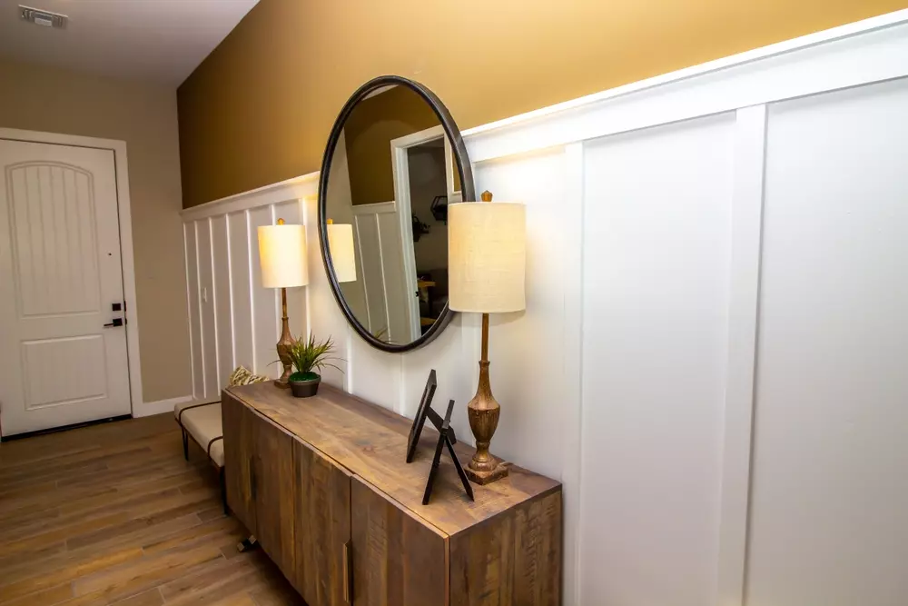 Espelho redondo acima de um móvel de madeira no corredor de entrada de um imóvel.
