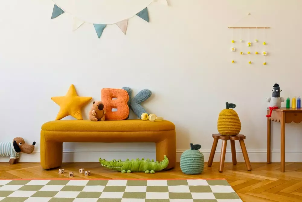 Decoração infantil com almofadas em formato de estrela, letras de pelúcia, brinquedos de pelúcia, cobertor com padrão de xadrez, e elementos decorativos coloridos na parede, criando um ambiente sensorial e visual atrativo para crianças.