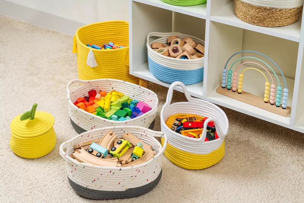Cestos de brinquedos coloridos com carros, blocos de montar e acessórios diversos, ideal para organização de brinquedos infantis em um espaço de quarto de criança.