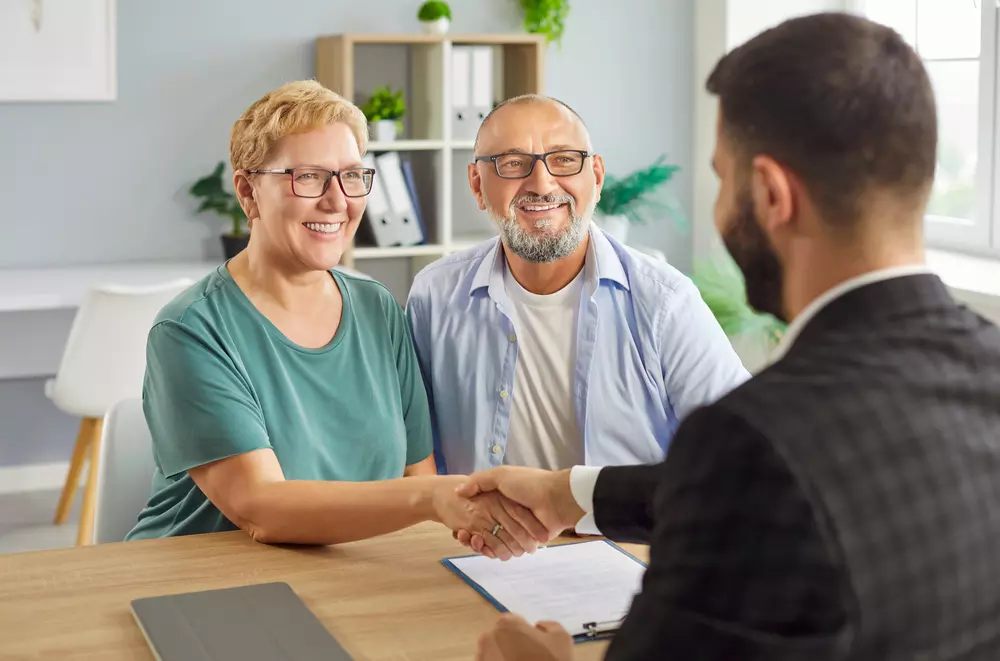 Casal de idosos sorrindo durante uma reunião de negócios com um jovem profissional, simbolizando sucesso e empreendedorismo na terceira idade.